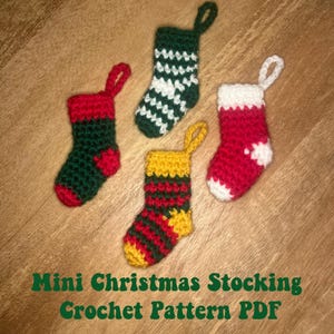 May include: Four mini crocheted Christmas stockings in red, green, yellow, and white. The stockings are hanging from a wooden surface.  Mini Christmas Stocking Crochet Pattern PDF