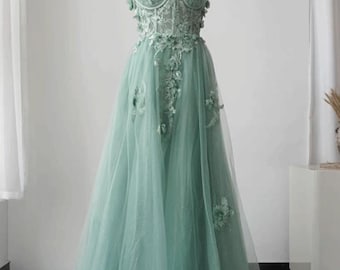 Puede incluir: Un vestido de fiesta verde menta con un escote asimétrico y adornos florales. El corpiño presenta detalles de encaje intrincados, y la falda es de tul fluido. El texto "ANDREASDEDesign" es visible.