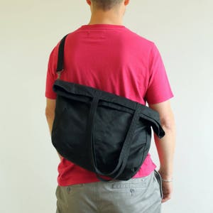 Puede incluir: Un bolso de hombro de lona negra con una correa larga ajustable y dos asas cortas. El bolso se lleva sobre el hombro y la parte superior est&aacute; doblada. El bolso est&aacute; hecho de un material duradero y es adecuado para el uso diario.