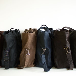 Puede incluir: Una colecci&oacute;n de bolsos de hombro en varios colores, incluyendo marr&oacute;n, negro y azul marino. Cada bolso tiene una correa larga y ajustable y un asa superior. Los bolsos est&aacute;n hechos de un material resistente.
