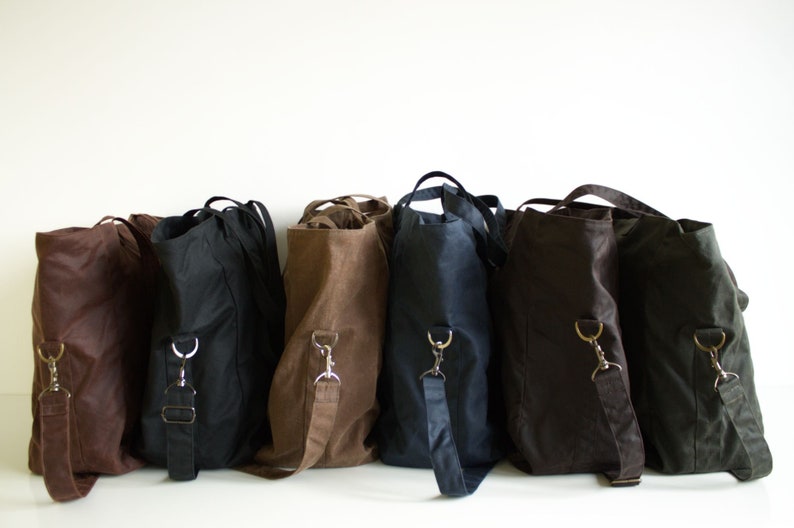 Puede incluir: Una colecci&oacute;n de bolsos de hombro en varios colores, incluyendo marr&oacute;n, negro y azul marino. Cada bolso tiene una correa larga y ajustable y un asa superior. Los bolsos est&aacute;n hechos de un material resistente.