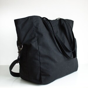 Puede incluir: Un bolso tote negro grande con dos asas largas y una correa de hombro desmontable. El bolso est&aacute; hecho de una tela resistente y presenta un dise&ntilde;o simple y minimalista. El bolso tiene forma rectangular y un interior espacioso.