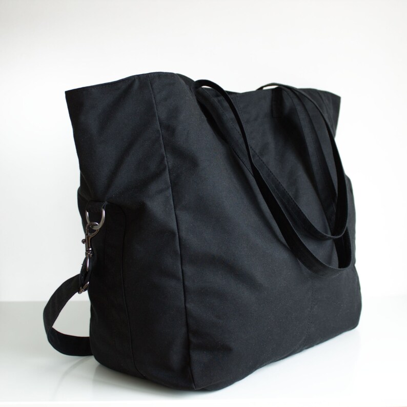 Puede incluir: Un bolso tote negro grande con dos asas largas y una correa de hombro desmontable. El bolso est&aacute; hecho de una tela resistente y presenta un dise&ntilde;o simple y minimalista. El bolso tiene forma rectangular y un interior espacioso.