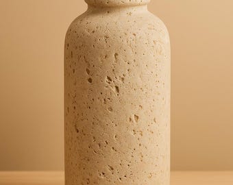 Puede incluir: Un jarrón beige texturizado con cuerpo cilíndrico y cuello estrecho. El jarrón tiene una superficie rugosa y porosa y está sobre una estantería de madera. El fondo es de color beige liso. Este jarrón decorativo es adecuado para la decoración del hogar.