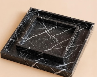 May include: Three square black marble trays with white veining are nested together. The trays are of different sizes, with the largest at the bottom and the smallest on top. The trays have a raised edge.