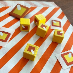 May include: Six yellow wooden cubes with a red and white symbol on each side. The cubes are on a white and orange striped surface.