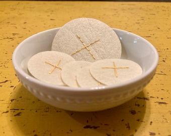May include: A white bowl filled with round, white communion wafers with gold crosses.