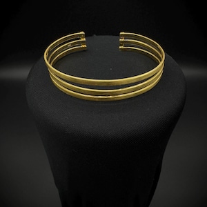 May include: A gold-toned triple-band choker necklace. The necklace is made of three thin bands of metal that are connected together. The bands are smooth and have a polished finish.