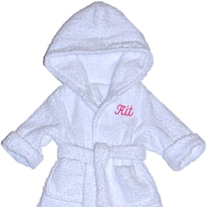 May include: White hooded bathrobe with a pink embroidered name "Kit" on the front. The robe has a tie belt and a pocket.