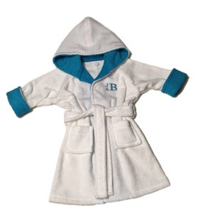 May include: White hooded baby bathrobe with teal blue trim on the hood, cuffs, and collar. The robe has a matching belt, two front pockets, and an embroidered "B" on the chest. Made of soft, absorbent material.