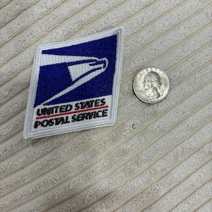 May include: A rectangular patch featuring the United States Postal Service logo, a blue eagle head and the words "UNITED STATES POSTAL SERVICE" in red and white. A US quarter coin is next to the patch.