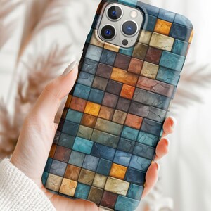 May include: A phone case with a mosaic pattern of blue, brown, and orange squares. The case has a camera cutout and a white border.