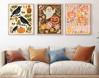 May include: Three framed Halloween-themed art prints. The prints feature illustrations of crows, skulls, pumpkins, ghosts, and flowers in a retro style. The color palette includes orange, brown, and cream.
