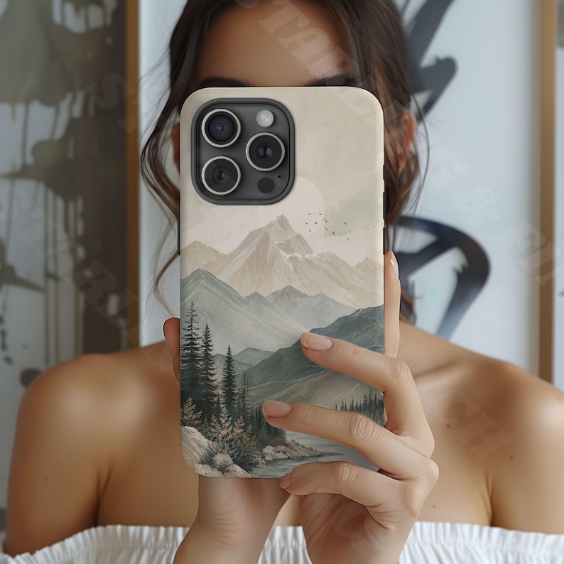 K&ouml;nnte beinhalten: Eine Smartphone-H&uuml;lle mit einer gedruckten Landschaftsillustration von geschichteten Gebirgsz&uuml;gen in ged&auml;mpften Beige- und Salbeigr&uuml;nt&ouml;nen, mit einem dichten Kiefernwald im Vordergrund und einer blassen Sonne am Himmel &uuml;ber den Gipfeln.