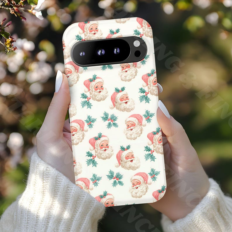 May include: A phone case featuring a repeating pattern of Santa Claus faces with pink hats and holly sprigs on a cream background. The case has a camera cutout and is held in a person's hands.
