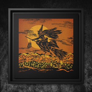 May include: A framed Halloween art print. The image shows a silhouetted witch on a broomstick against an orange sky with a full moon. The landscape below features mountains, trees, and a small building, all in orange and black.