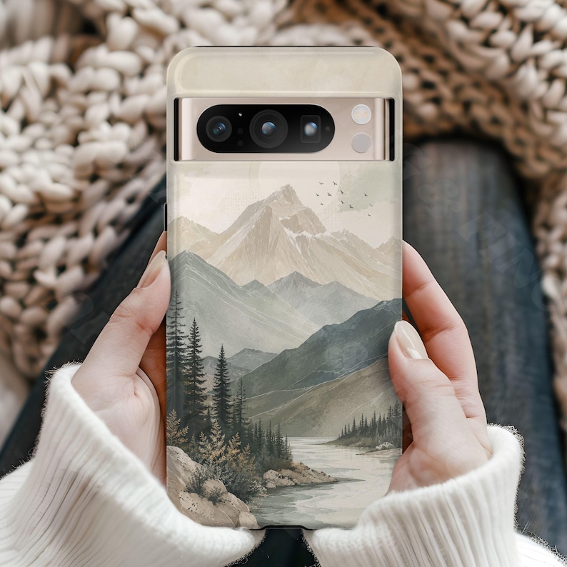K&ouml;nnte beinhalten: Eine Smartphone-H&uuml;lle mit einer Landschaftsillustration von schneebedeckten Bergen, einem gewundenen Fluss und einem dichten Kiefernwald in gedeckten Beige-, Salbeigr&uuml;n- und Graut&ouml;nen. Das Design zeigt zudem einen kleinen Vogelschwarm am Himmel.