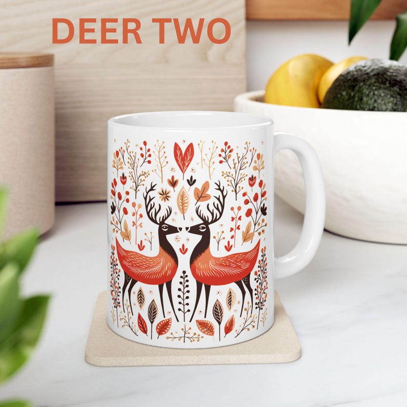 May include: White ceramic mug with a colorful illustration of two deer with antlers facing each other in a forest setting. The mug has a handle and the text "DEER TWO" is printed above the image.