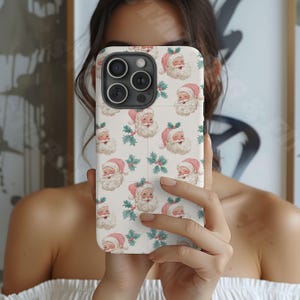 May include: A white phone case featuring a repeating pattern of Santa Claus faces with pink hats and holly sprigs. The case has a glossy finish and a camera cutout.