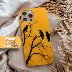 May include: A yellow phone case featuring a black silhouette of a tree with three crows perched on its branches. The case has a glossy finish and is designed for iPhone, Pixel, and Samsung phones. The text "iPhone Pixel Samsung" is on the left side.