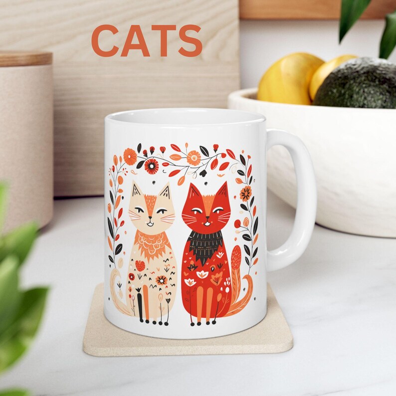 May include: White ceramic mug with a colorful illustration of two cats with floral accents. The text "CATS" is printed in bold letters above the image.