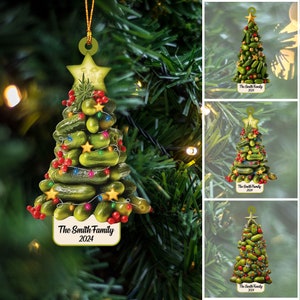 May include: A Christmas tree ornament shaped like a Christmas tree made of pickles, with red berries, green lights, and gold stars. The ornament has a white tag with the text "The Smith Family 2024".