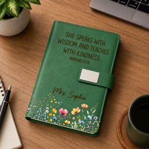 May include: A green leather journal with the text "SHE SPEAKS WITH WISDOM AND TEACHES WITH KINDNESS PROVERBS 31:26" and "Mrs. Sophia". The journal features a floral design along the bottom edge and a magnetic closure.