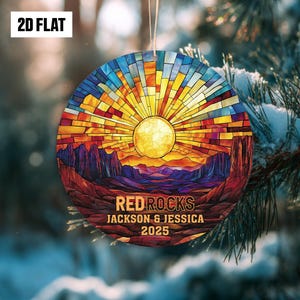 May include: A round Christmas ornament with a stained-glass design featuring a sunset over a canyon. The ornament has the text "RED ROCKS JACKSON & JESSICA 2025" and "2D FLAT". The color palette includes shades of red, orange, yellow, blue, and purple.