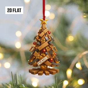 May include: A wooden Christmas tree ornament with tools and red ornaments. The tree is made of wooden planks and decorated with saws, hammers, and a star. The name "JACKSON" is displayed on a wooden sign. The ornament hangs from a red ribbon.