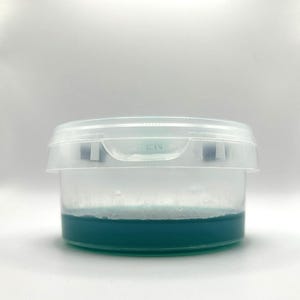 May include: A clear plastic container with a blue liquid inside. The container has a lid with the word "OPEN" printed on it.