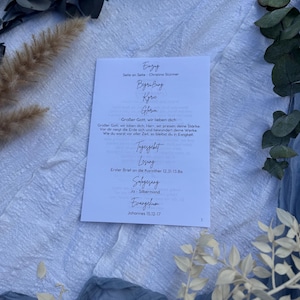 Peut inclure: Une carte blanche avec du texte allemand, dont "Eingay" et "Begrüßung", est entourée de verdure et de tissu. Le texte de la carte comprend des phrases comme "Großer Gott, wir lieben dich" et des références aux écritures. L'esthétique générale est douce et naturelle.
