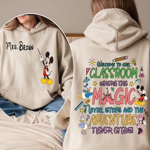 May include: Beige hoodie with a Mickey Mouse design on the front and a colourful graphic on the back that says "Welcome to our classroom where the magic never stops and the adventure never ends!"