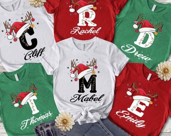 May include: Five white t-shirts with different letters and names printed on them. Each letter has a red Santa hat and reindeer antlers. The letters are C, R, M, T, and E. The names are Cliff, Rachel, Mabel, Thomas, and Emily.