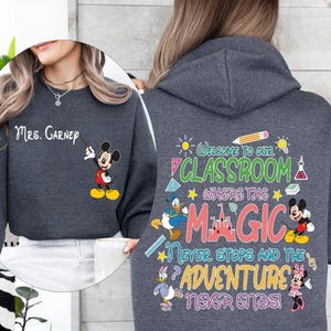 May include: A dark grey hooded sweatshirt with a Mickey Mouse design and the text "Welcome to our classroom where the magic never stops and the adventure never ends!" printed on the front. The back of the sweatshirt has the text "Mrs. Garney" printed on it.