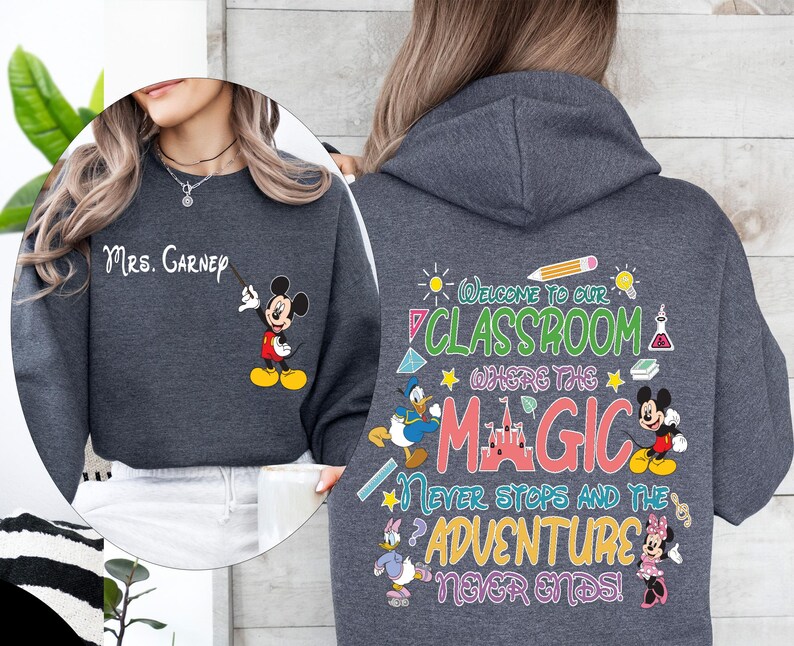 May include: A dark grey hooded sweatshirt with a Mickey Mouse design and the text "Welcome to our classroom where the magic never stops and the adventure never ends!" printed on the front. The back of the sweatshirt has the text "Mrs. Garney" printed on it.