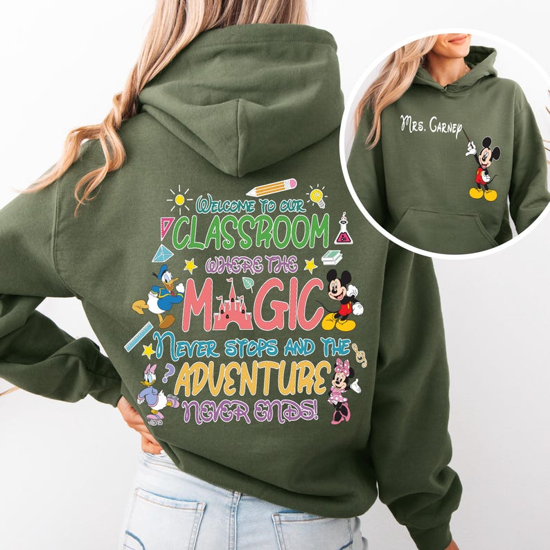 May include: Green hooded sweatshirt with a colourful graphic print featuring Mickey Mouse, Minnie Mouse, Donald Duck, and a castle. The text reads "Welcome to our classroom where the magic never stops and the adventure never ends!"