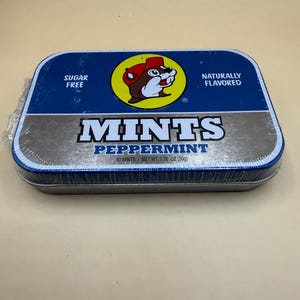 May include: A rectangular tin of peppermint mints. The tin is blue and silver with the text "MINTS PEPPERMINT" in large white letters. The tin also features a cartoon beaver in a yellow circle and the words "SUGAR FREE" and "NATURALLY FLAVORED".