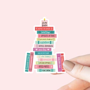May include: A sticker with a stack of books, each book title is a different romance trope. The titles include "Slow Burn", "Enemies to Lovers", "Road Trip", "Opposites Attract", "Second Chance", "Instalove", "Office Romance", "One Bed", "Love at First Sight", "Love Triangle", "Amnesia", "Holiday Romance", "Fated Mates", and "Fake Dating".