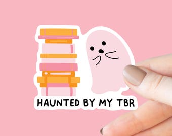 May include: A pink ghost sticker with a stack of books behind it. The sticker says "Haunted by my TBR".