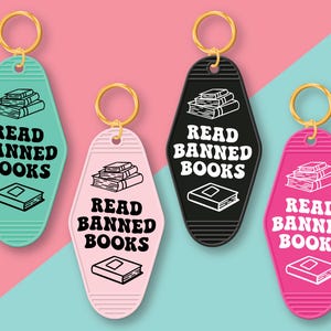 May include: Four keychains shaped like motel room keys with the text "Read Banned Books" in black and white. The keychains are in turquoise, black, pink, and white.