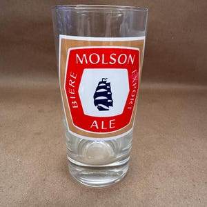 May include: A white ceramic mug with a black handle and the text "But First, Coffee" in a bold, black font. The mug is set against a blurred background, suggesting a cozy setting.