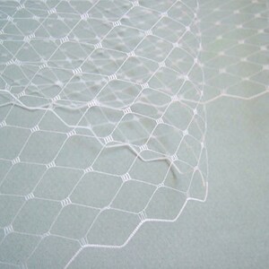 May include: White bridal veil made of fine netting with a diamond pattern. The veil is delicate and sheer, with a soft, flowing texture.