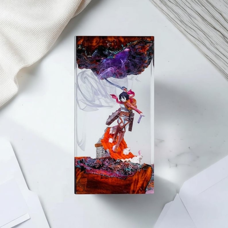 Puede incluir: Escultura rectangular de resina con una figura de anime detallada en acci&oacute;n, con una espada y una capa ondeante. La figura se encuentra sobre un fondo de colores arremolinados, incluyendo naranja, morado y marr&oacute;n.