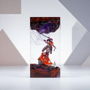 Puede incluir: Escultura de resina que presenta una figura de anime con una espada, sobre una base texturizada marr&oacute;n rojizo. Elementos morados y blancos arremolinados completan la escena, todo encerrado en un bloque rectangular transparente.