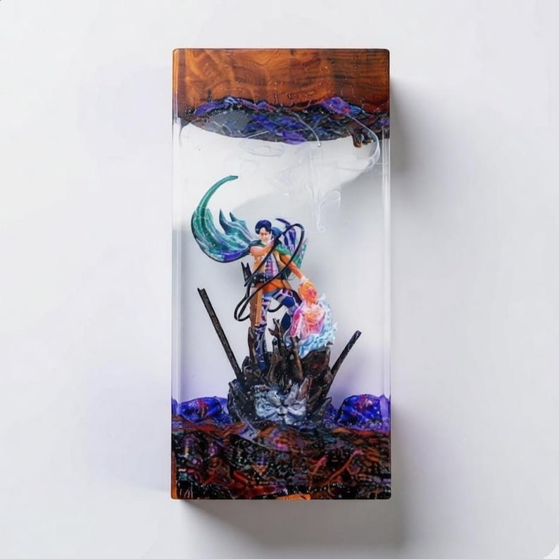 Puede incluir: Una pieza de arte de resina rectangular con una figura detallada de un personaje con una capa fluida y otra figura. La resina tiene una parte superior de madera y una base con patrones coloridos y arremolinados. Las figuras est&aacute;n en el centro de la resina transparente.