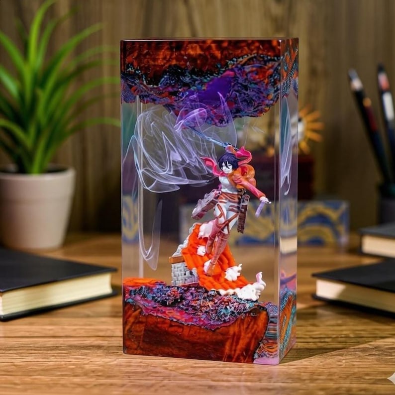 Puede incluir: Una pieza de arte rectangular de resina con una figura de un personaje en una pose din&aacute;mica. El bloque de resina tiene un dise&ntilde;o colorido y en capas con tonos rojos, naranjas y morados. La figura lleva un atuendo rojo y blanco.
