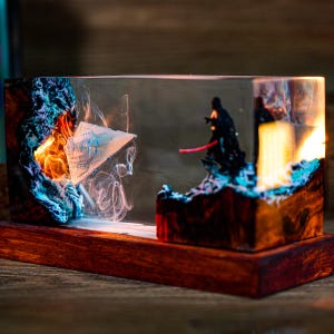 Könnte beinhalten: Ein Star Wars-Kunstwerk aus Harz mit einer detaillierten Darstellung von Darth Vader mit einem roten Lichtschwert und einem Raumschiff. Das Kunstwerk ist in einem transparenten Harzblock eingeschlossen, der auf einem Holzsockel steht, mit leuchtenden Farben und komplizierten Details.