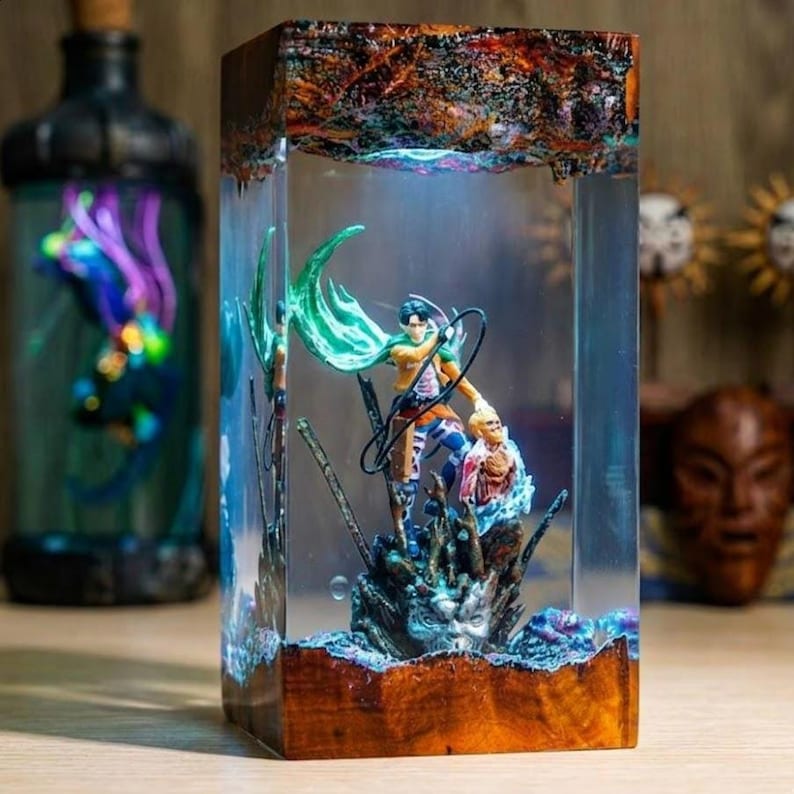 Puede incluir: Una pieza de arte de resina rectangular con una figura de anime detallada con una capa verde y un compa&ntilde;ero. La obra de arte est&aacute; encerrada en resina transparente con una base de madera y una parte superior texturizada, creando una exhibici&oacute;n &uacute;nica. La pieza est&aacute; iluminada con luz azul.