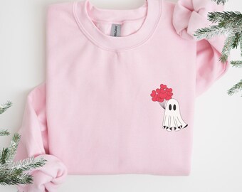 Puede incluir: Sudadera rosa claro con un diseño de fantasma de dibujos animados sosteniendo globos rojos en forma de corazón. El fantasma tiene dos ojos negros y un cuerpo blanco. Cuello redondo.