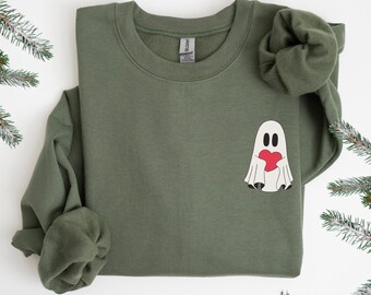 Puede incluir: Una sudadera verde con un fantasma blanco que sostiene un corazón rojo. El fantasma está en el centro de la sudadera.